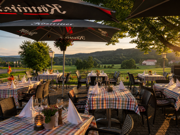 Gemütliches Restaurant im Freien mit Tischen und Blick auf eine grüne Landschaft.