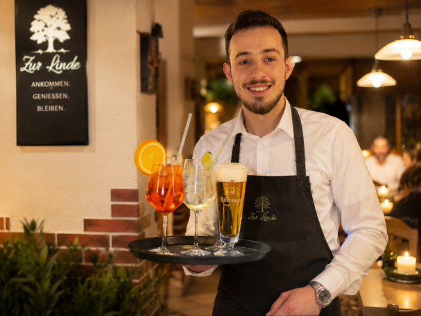 Ein Kellner trägt ein Tablett mit verschiedenen Getränken in einem Restaurant.